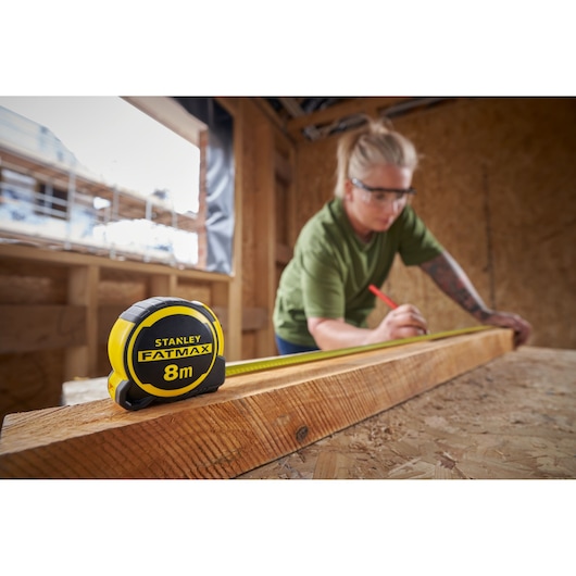 STANLEY FMHT33102-0 rolmaat 8m in gebruik, op een houten balk in een bouwomgeving.