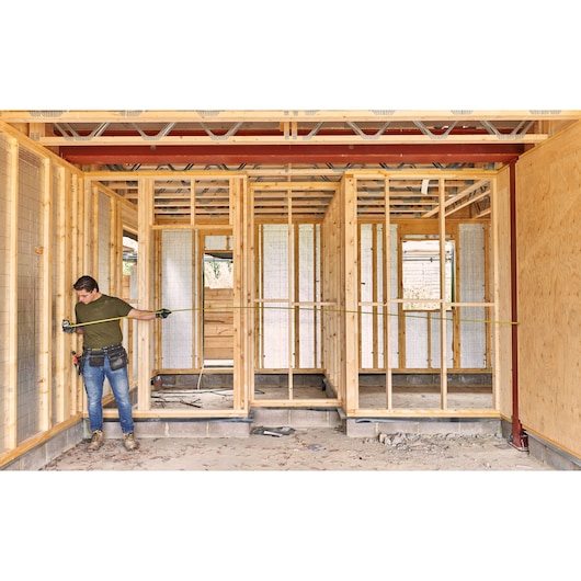 STANLEY FMHT38217-0 rolmaat gebruikt door een werknemer op houten bouwplaats voor het opmeten van een wandframe.