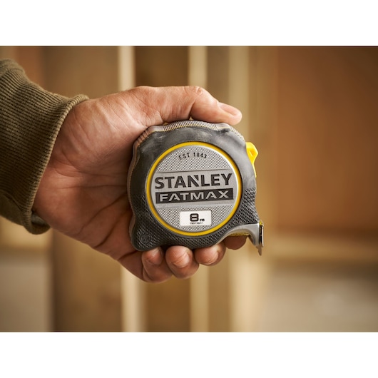 Foto van STANLEY FMHT38217-0 FATMAX rolmaat, 8m lang, vastgehouden in hand, zwarte en gele behuizing.