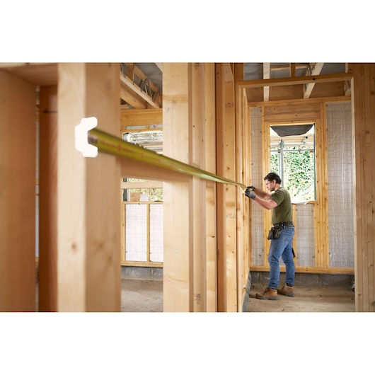 STANLEY FMHT38232-0 rolmaat uitgeschoven door werknemer in houten huisframe, zijaanzicht, bouwplaats.