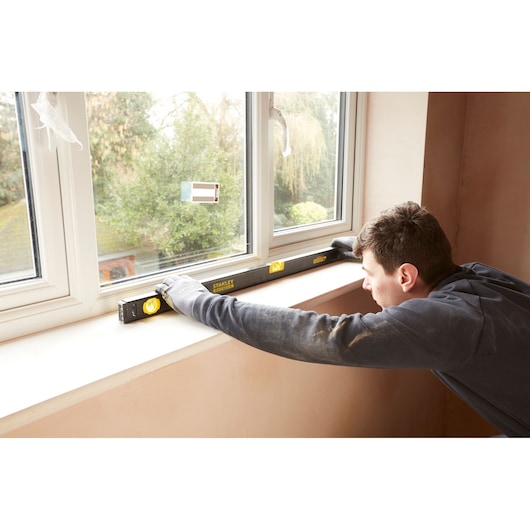 Stanley FMHT42447-1 waterpas gebruikt door arbeider met handschoenen op vensterbank, binnenomgeving.