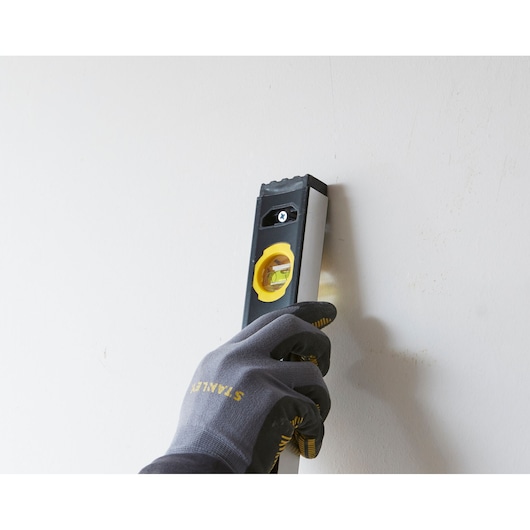 Foto van STANLEY FMHT42447-1 waterpas, vastgehouden door een gehandschoende hand tegen de muur.