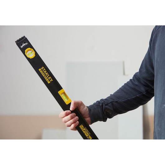 Foto van een persoon met een STANLEY FATMAX waterpas, SKU FMHT42554-1, zwart en geel, gebruikt in de bouw.