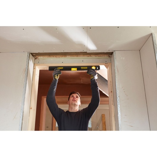 Persoon gebruikt STANLEY FMHT42554-1 waterpas om deuropening uit te lijnen tijdens de bouw.