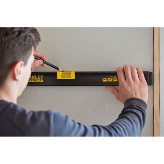 Foto van STANLEY FMHT42554-1 waterpas in gebruik op een muur, persoon markeert lijn met potlood.