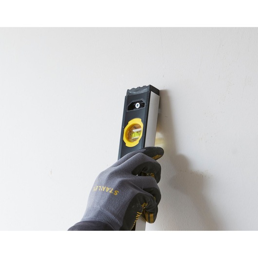 STANLEY FMHT42559-1 waterpas wordt verticaal tegen een muur gehouden door een gehandschoende hand, zijaanzicht.