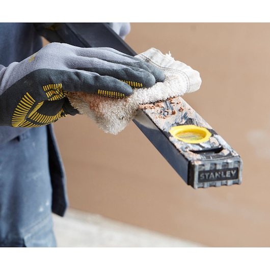 Foto van een gehandschoende hand die een met vuil bedekt STANLEY FMHT42561-1 waterpas schoonmaakt, close-up.