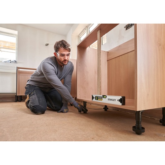 Stanley FMHT43671-1 waterpas gebruikt onder houten kast bij installatie, binnenscène.