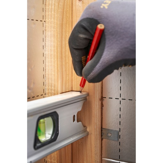 STANLEY FMHT43671-1 waterpas tegen hout, gehandschoende hand markeert met rode potlood, zijaanzicht.