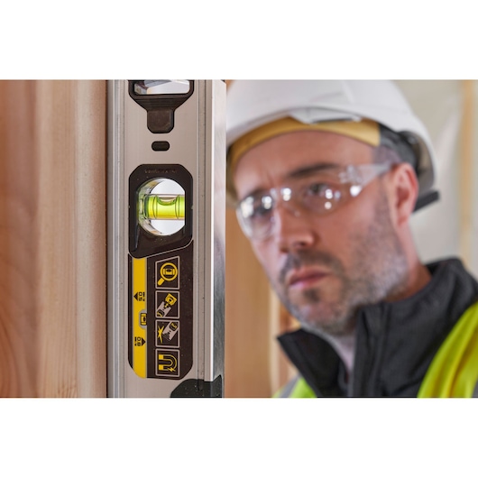 STANLEY FMHT43671-1 waterpas met gele accenten, verticale weergave naast hout, vervaagde werker op de achtergrond.