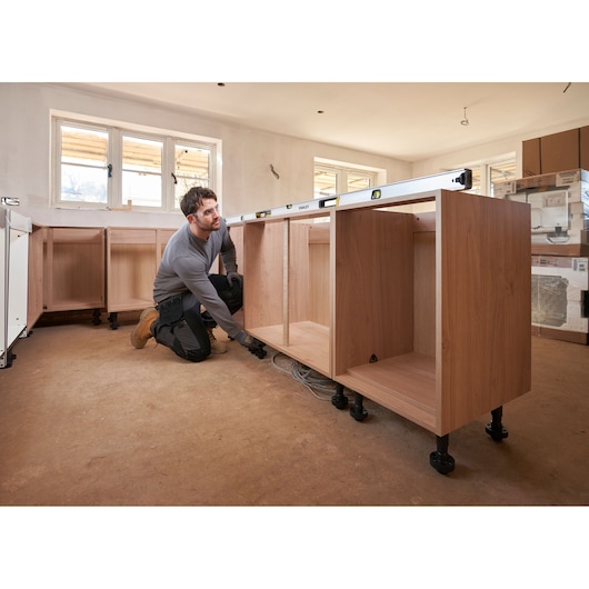 Foto van STANLEY FMHT43679-1 waterpas op houten keukenkasten tijdens installatie, monteur stelt de basis af.