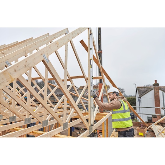 STANLEY FMHT43679-1 waterpas gebruikt door werker met veiligheidshesje op bouwplaats met houten frame.