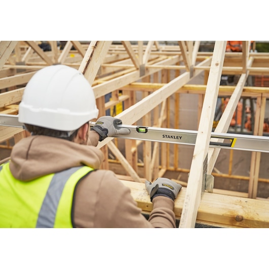 STANLEY FMHT43679-1 waterpas gebruikt door werknemer met handschoenen en helm op houten dakconstructie.