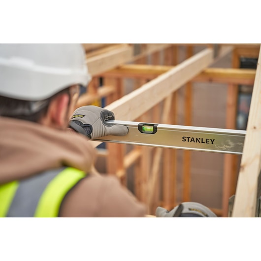 STANLEY FMHT43679-1 waterpas vastgehouden door een medewerker met handschoenen, gebruikt voor het nivelleren van een houten frame op een bouwplaats.