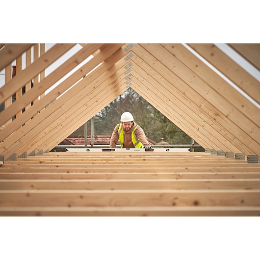 STANLEY FMHT43680-1 waterpas in gebruik op houten dakconstructie, werknemer met veiligheidshesje en helm.