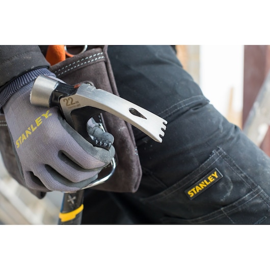 Marteau STANLEY FMHT51367-2 tenu par une main gantée près d’un pantalon de travail avec logo STANLEY, vue rapprochée.