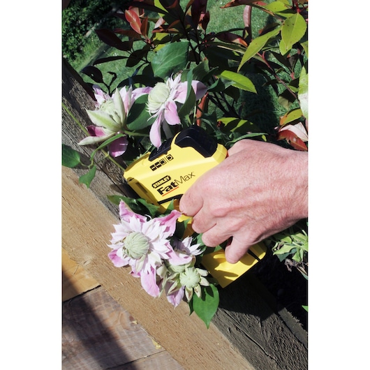 Agrafeuse STANLEY FMHT6-70411 FatMax jaune tenue à la main près de fleurs roses en extérieur.