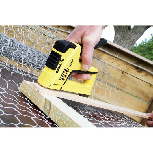 STANLEY FMHT6-70411 agrafeuse manuelle jaune fixant un grillage sur du bois, vue de côté, extérieur.