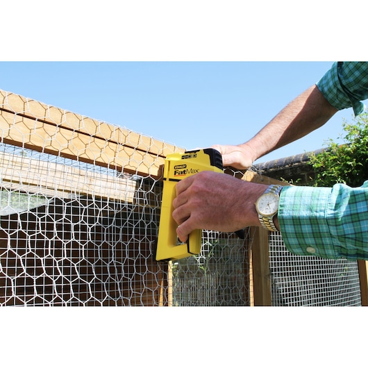 Agrafeuse STANLEY FMHT6-70411 fixant un grillage métallique à un cadre en bois à l'extérieur.