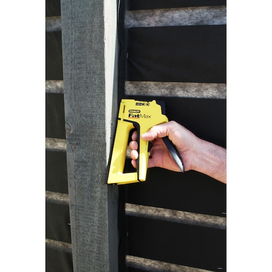 Agrafeuse manuelle STANLEY FMHT6-70411 jaune, utilisée contre une poutre en bois.