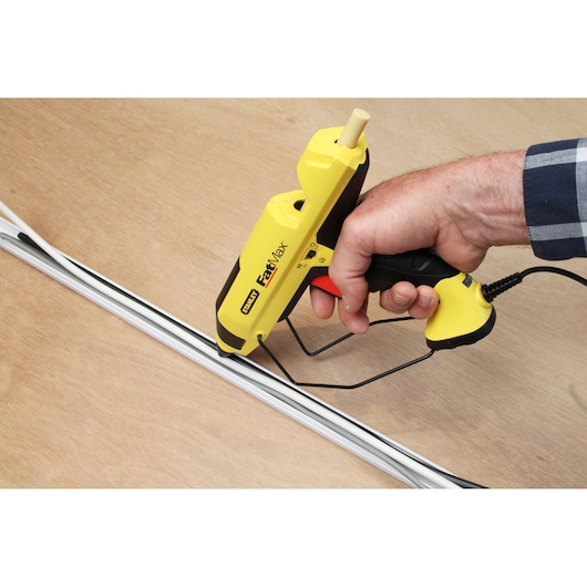 STANLEY FMHT6-70418 pistolet à colle jaune utilisé pour coller une baguette blanche sur surface en bois.