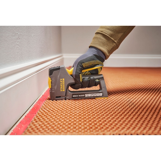 Agrafeuse multi-tacker Stanley FMHT6-70868 utilisée, tenue par une main gantée fixant un tapis près du mur.
