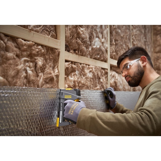 STANLEY FMHT6-70868 agrafeuse utilisée sur isolant par un ouvrier ganté, vue sur chantier.