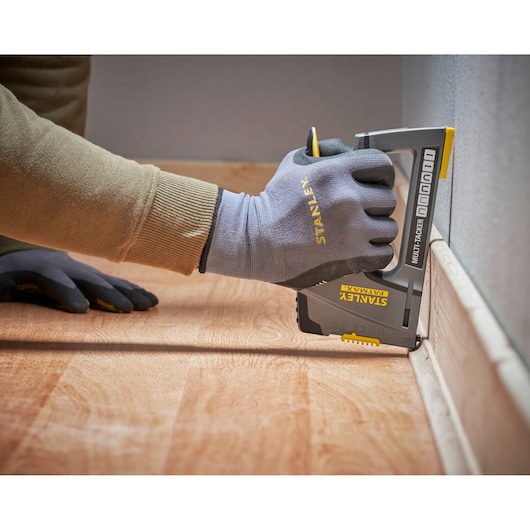 Photo d'une main avec des gants Stanley utilisant un agrafeuse multiple STANLEY FMHT6-70868 sur une plinthe, angle latéral.