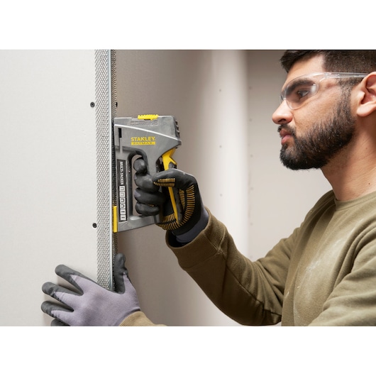 STANLEY FMHT6-70868 agrafeuse utilisée sur un mur en plaques de plâtre, gros plan main gantée.