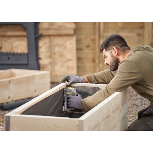 Agrafeuse STANLEY FMHT6-70868 utilisée pour fixer du tissu à l'intérieur d'un bac en bois en extérieur.