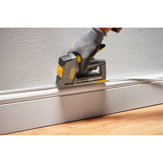 Photo du multi-tacker STANLEY FMHT6-70868 utilisé pour fixer une moulure au mur, tenu par une main gantée.
