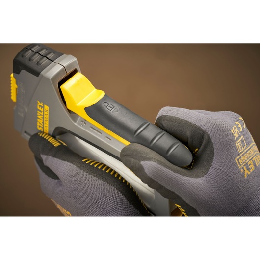 Photo de l’agrafeuse grise et jaune STANLEY FMHT6-70868 tenue par des mains gantées, vue rapprochée.