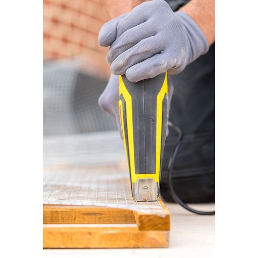 STANLEY FMHT6-75934 elektrische tacker close-up op draadgaas en hout, met handschoen bediende hand.