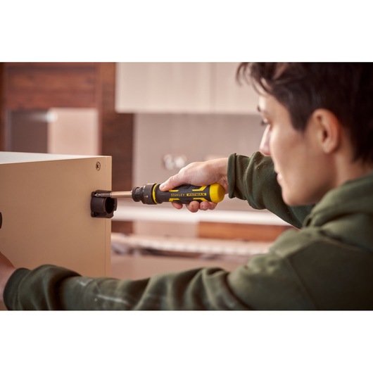 Stanley FMHT62692-0 tournevis utilisé pour assembler un meuble, poignée jaune et noire, environnement intérieur.