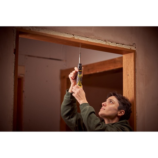 STANLEY FMHT62692-0 tournevis tenu verticalement lors de l'installation d'un cadre de porte, poignée jaune et noire visible.
