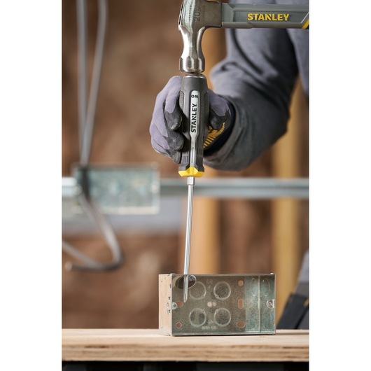 Tournevis et marteau Stanley utilisés sur un boîtier électrique en métal sur une surface en bois.