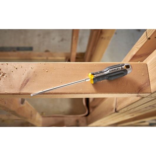 Stanley platte schroevendraaier met zwart-geel handvat op een houten balk in een werkplaats.
