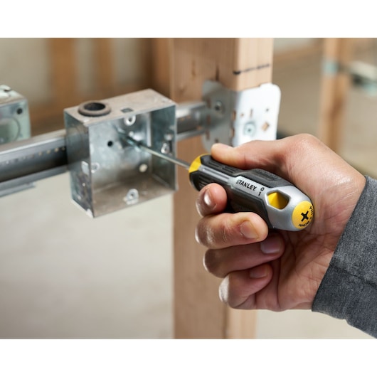 Hand gebruikt STANLEY kruiskopschroevendraaier om een schroef in een metalen doos op hout vast te draaien.