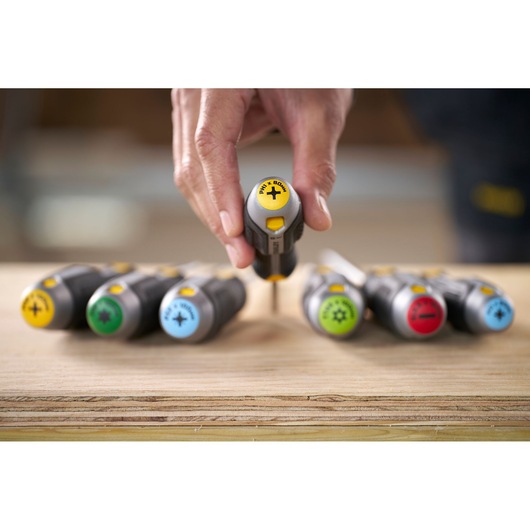 Hand houdt een Stanley-schroevendraaier met gekleurde grepen op een houten oppervlak.