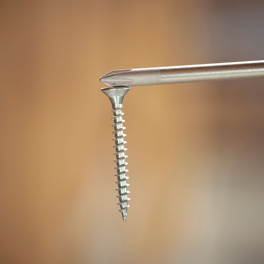 Close-up van een schroevendraaierpunt in een metalen schroef tegen een wazige bruine achtergrond.