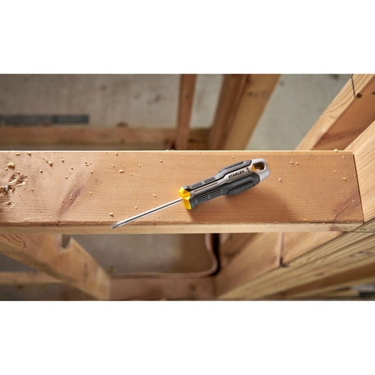 Stanley-schroevendraaier met zwart-gele grip ligt op een houten balk in een bouwomgeving.