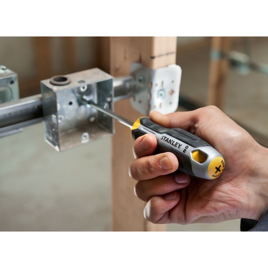Hand gebruikt een STANLEY kruisschroevendraaier om een schroef in een metalen elektrische doos te bevestigen.