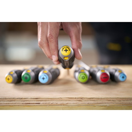Hand pakt een Stanley-schroevendraaier uit een set met gekleurde handvatten op hout.