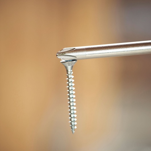 Close-up van een schroevendraaierpunt die een metalen schroef vasthoudt, achtergrond wazig.