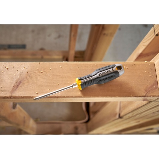 Stanley schroevendraaier met zwart-geel handvat op houten balk in bouwomgeving.