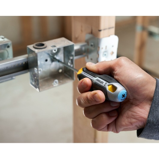 Main utilisant un tournevis Stanley pour fixer une vis dans un boîtier électrique métallique lors de l’installation.