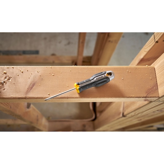 Tournevis Stanley à poignée noire et jaune posé sur une poutre en bois dans un chantier.