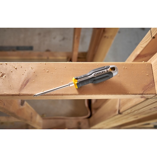 Tournevis Phillips Stanley à manche gris et jaune sur une poutre en bois sur un chantier.