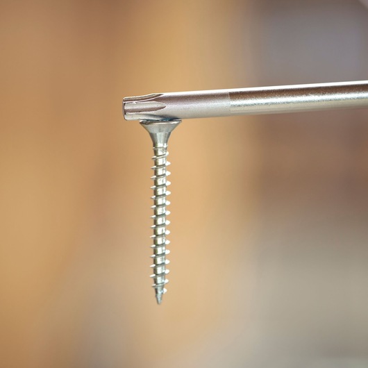 Close-up van een schroevendraaierbit in een metalen schroef met een wazige achtergrond.