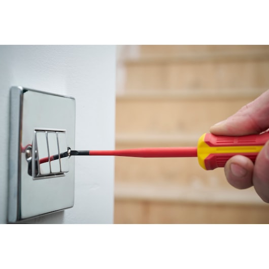 Tournevis isolé utilisé pour serrer une vis sur un interrupteur.